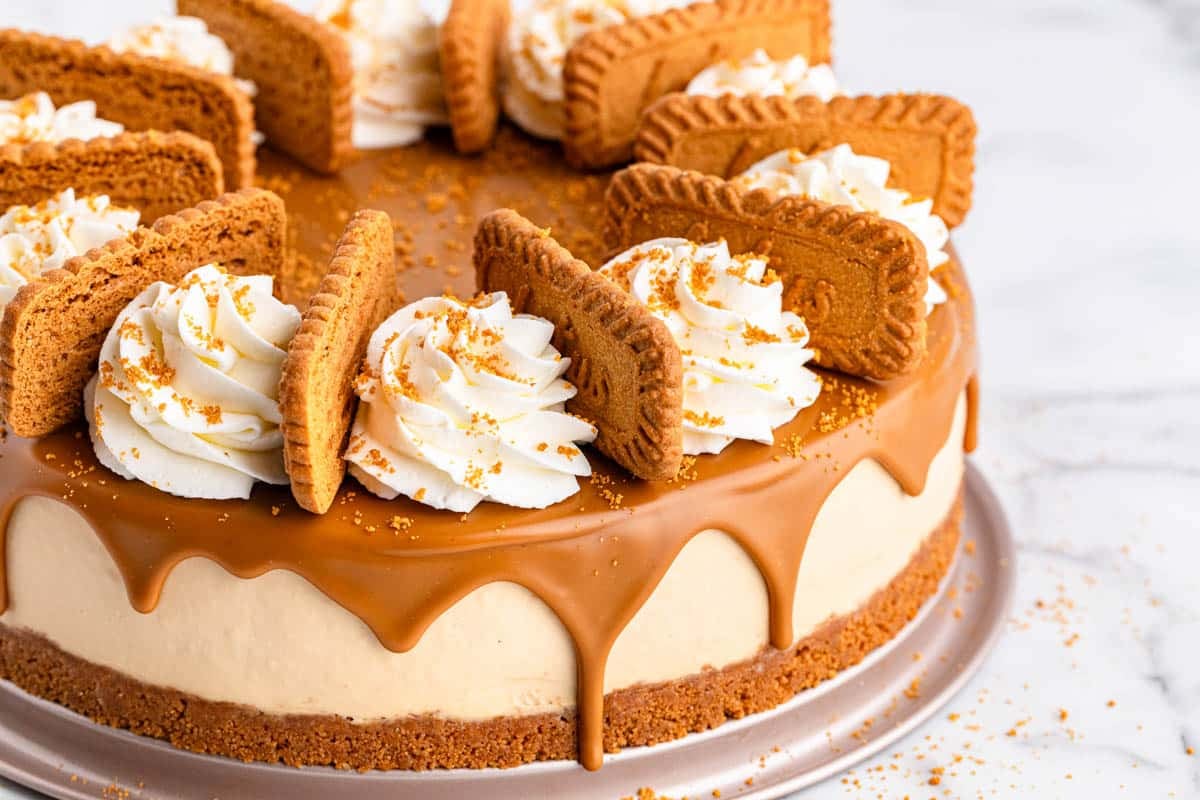 Cheesecake with caramel glaze, whipped cream, and cookies on top, placed on a silver platter.
