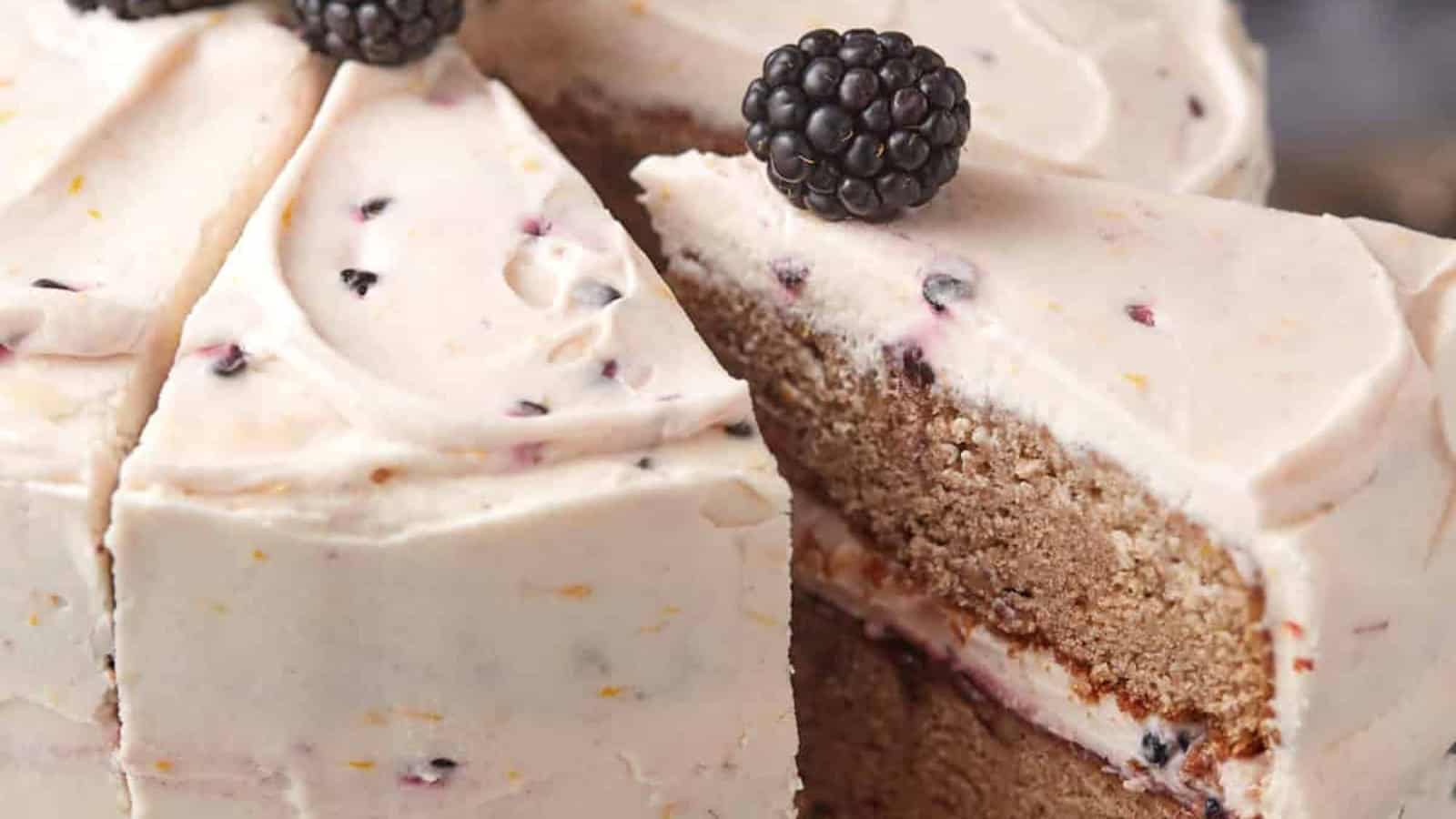 Sliced blackberry cake with creamy frosting, topped with whole blackberries.