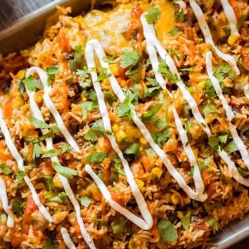 A tray of cheesy Mexican rice casserole topped with sour cream drizzle and fresh chopped cilantro.