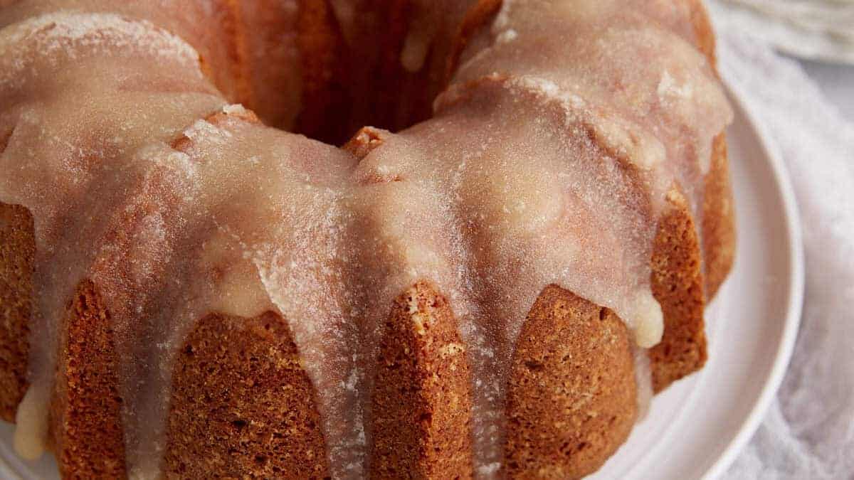 Close-up of a Bundt cake with a thick, white glaze drizzled on top, sitting on a white plate—evoking the charm of vintage cakes.