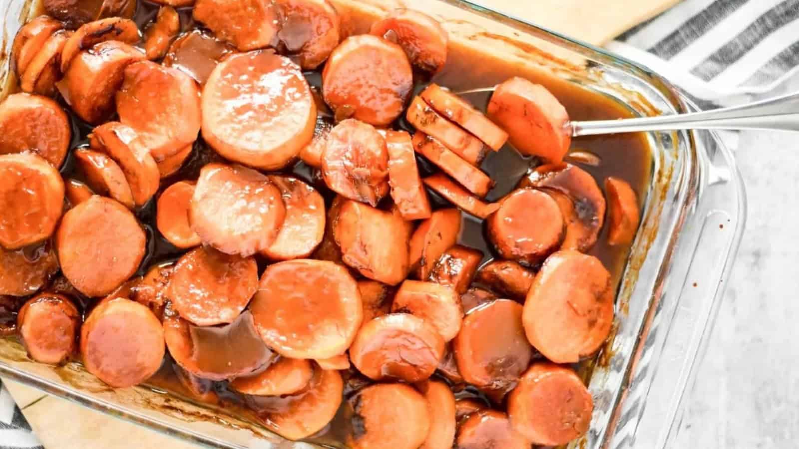 Sliced sweet potatoes in a glass dish, covered in a glossy brown glaze with a serving fork.