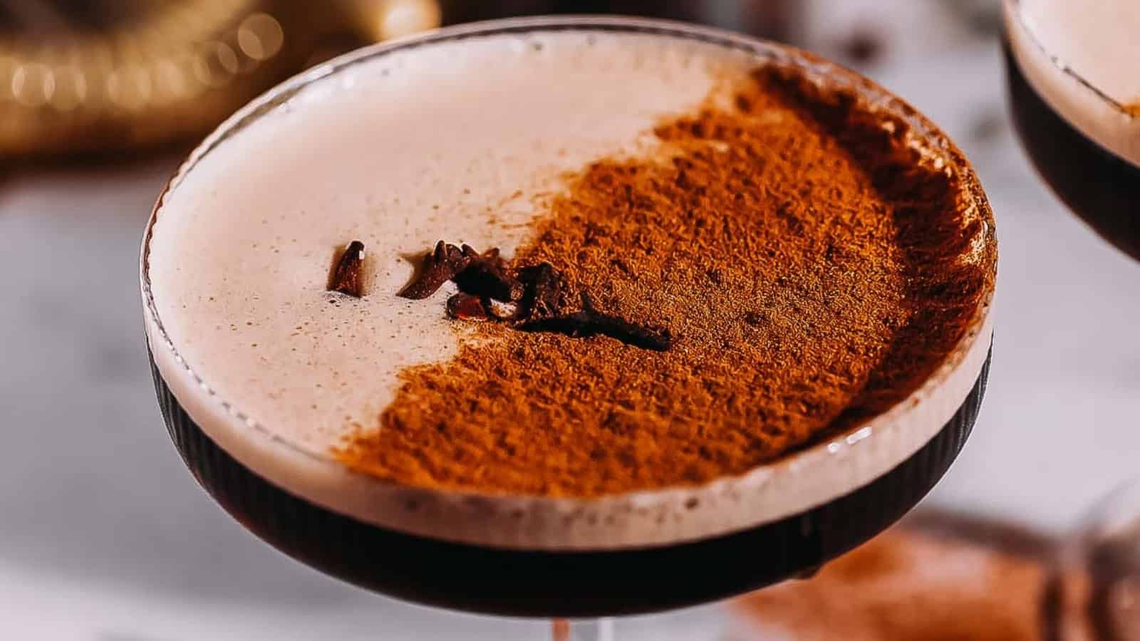 A close-up of a cocktail with frothy foam, topped with cinnamon powder and a few whole cloves.