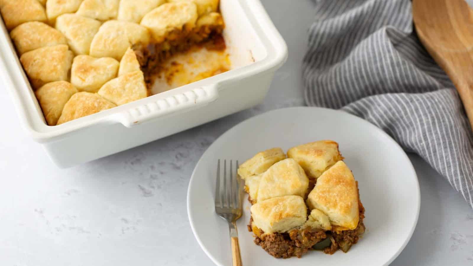 A serving of biscuit-topped casserole on a plate beside a baking dish with more casserole.