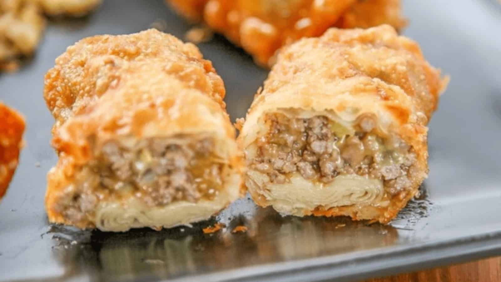 Close-up of a sliced, golden-brown, crispy egg roll filled with ground beef on a dark tray.