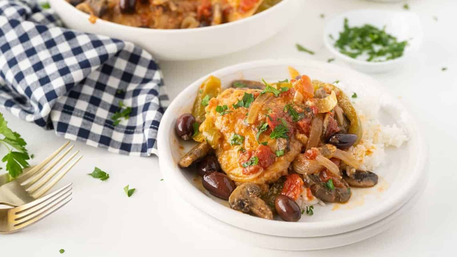 A plate of chicken cacciatore with olives, mushrooms, and rice, garnished with chopped parsley.