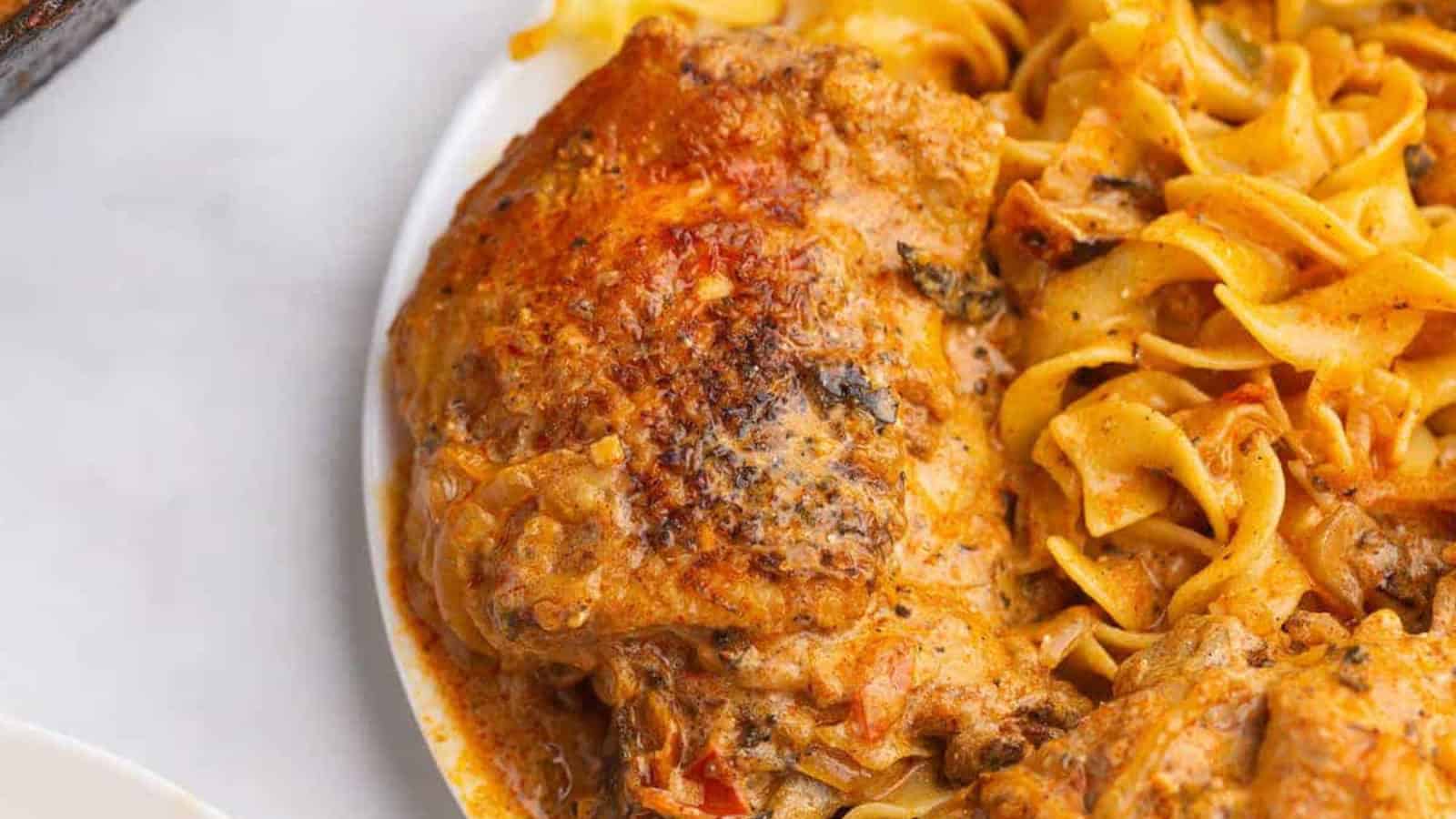 Chicken with creamy sauce and cooked egg noodles on a white plate.