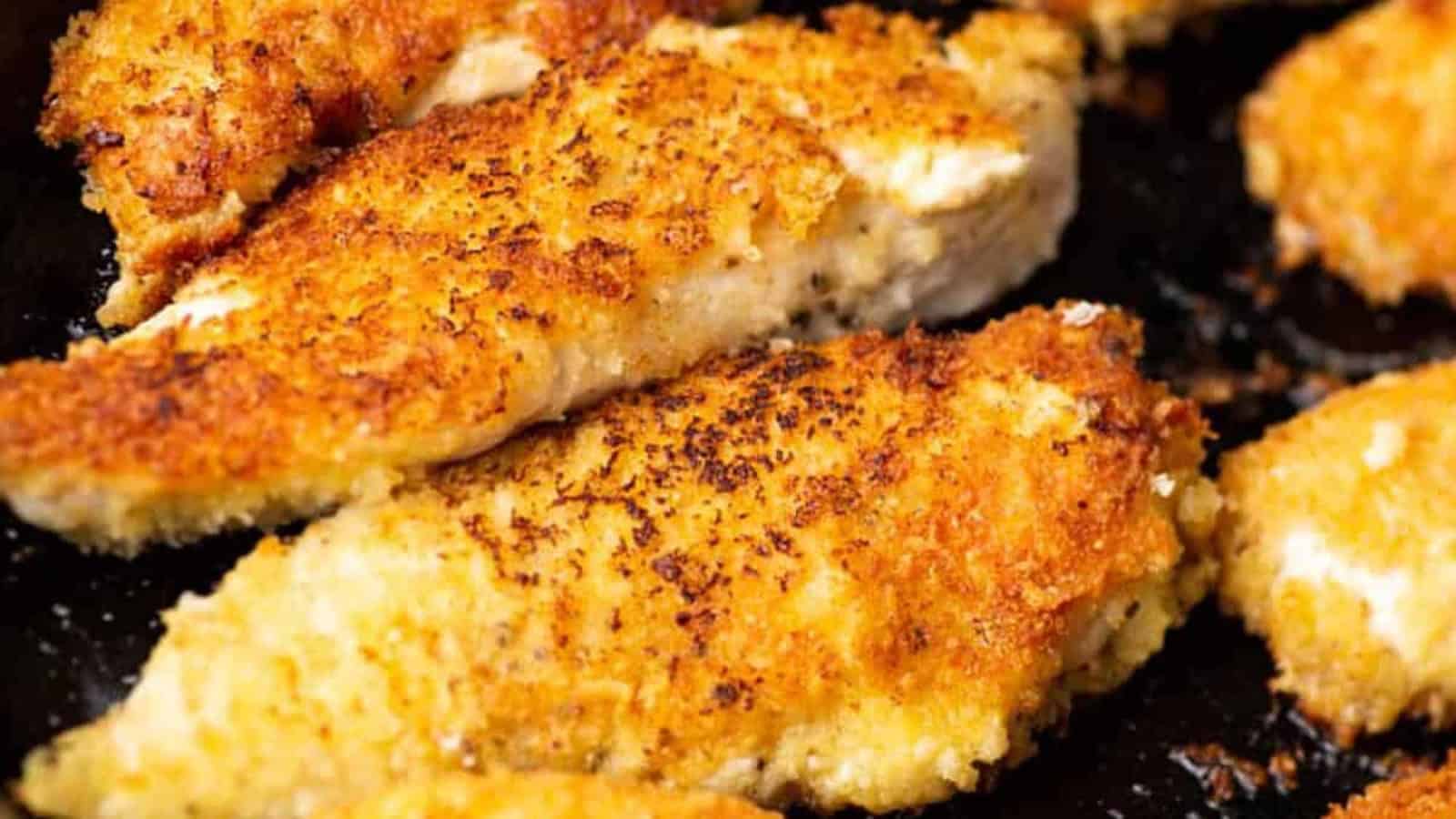 Close-up of golden, crispy breaded chicken tenders cooking on a skillet or baking sheet.