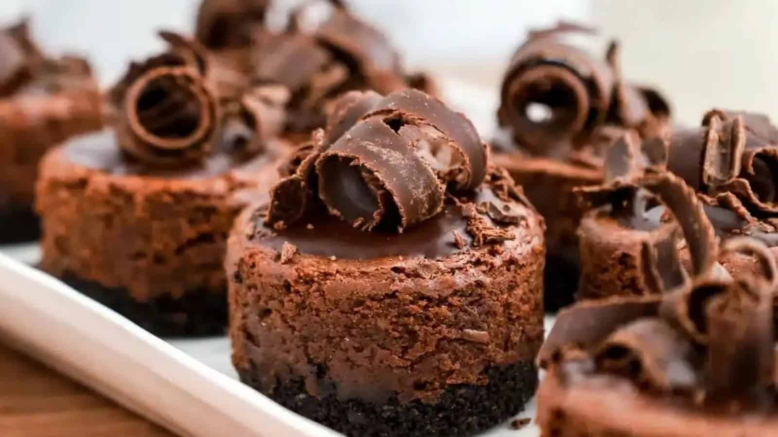 Mini chocolate cheesecakes topped with chocolate curls, arranged on a white platter.