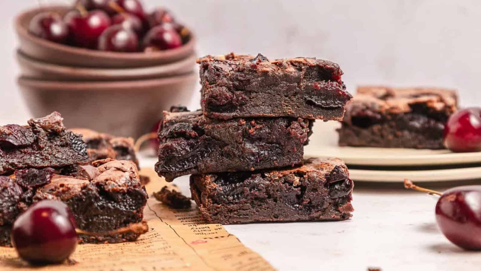 Three cherry brownies stacked with fresh cherries and bowls of cherries in the background.