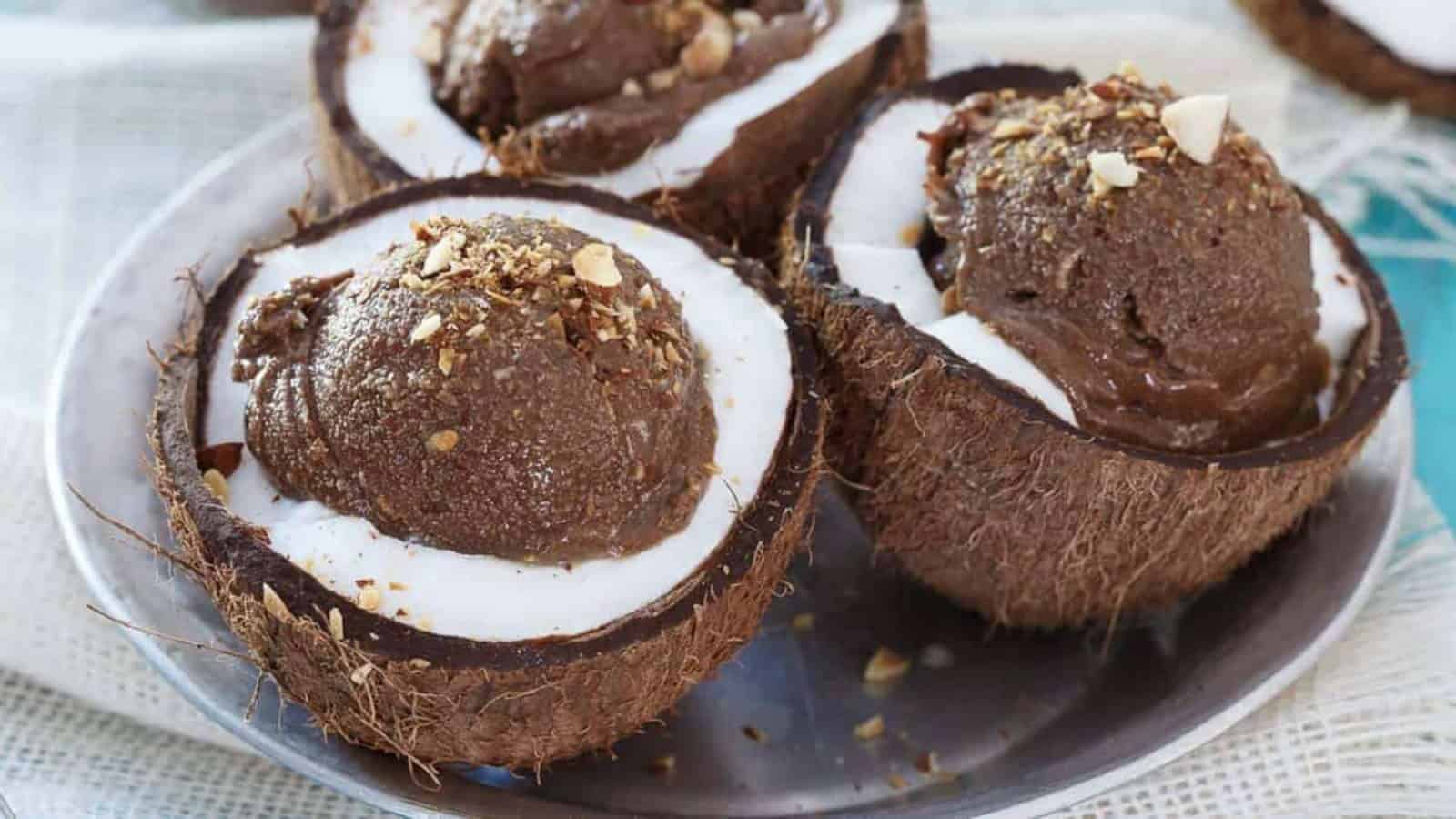 Chocolate ice cream served in coconut shells, topped with chopped nuts, on a metal plate.
