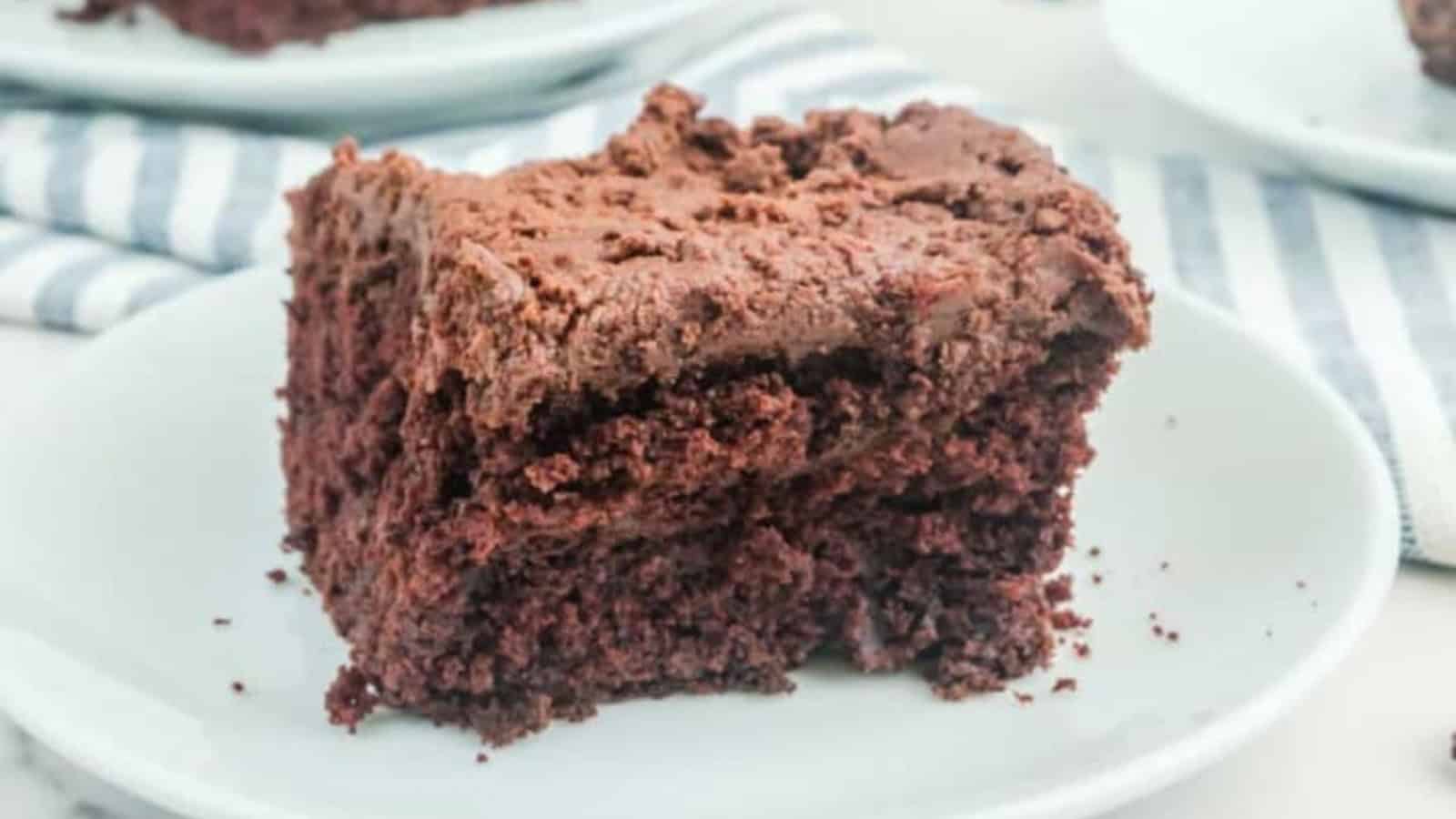 A slice of chocolate cake with chocolate frosting on a white plate.