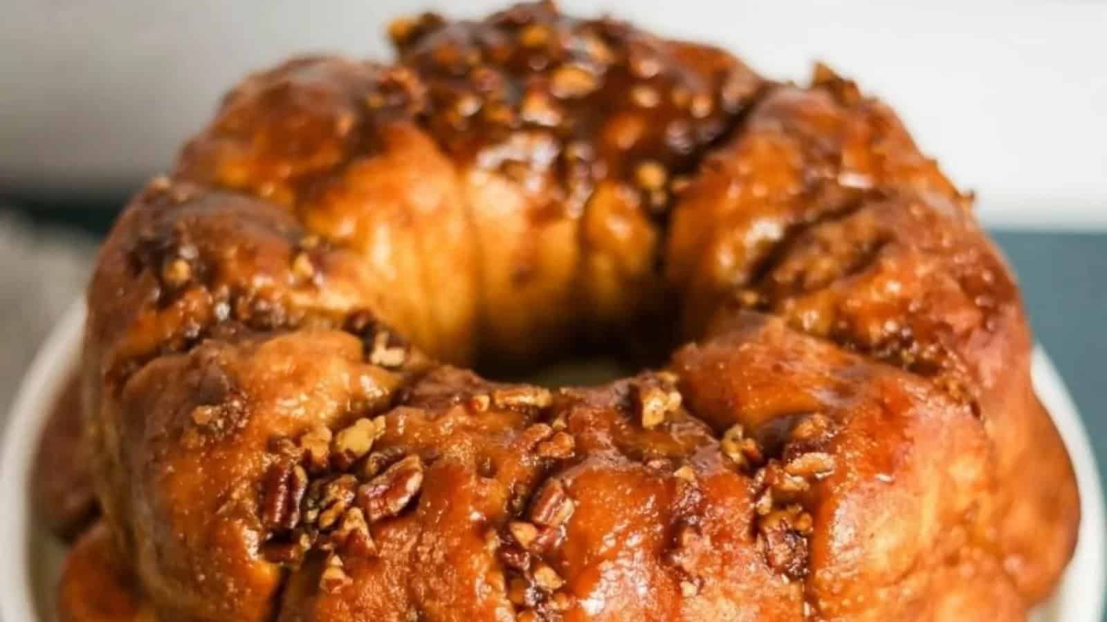 Round sticky bun coffee cake topped with glazed pecans on a white plate.