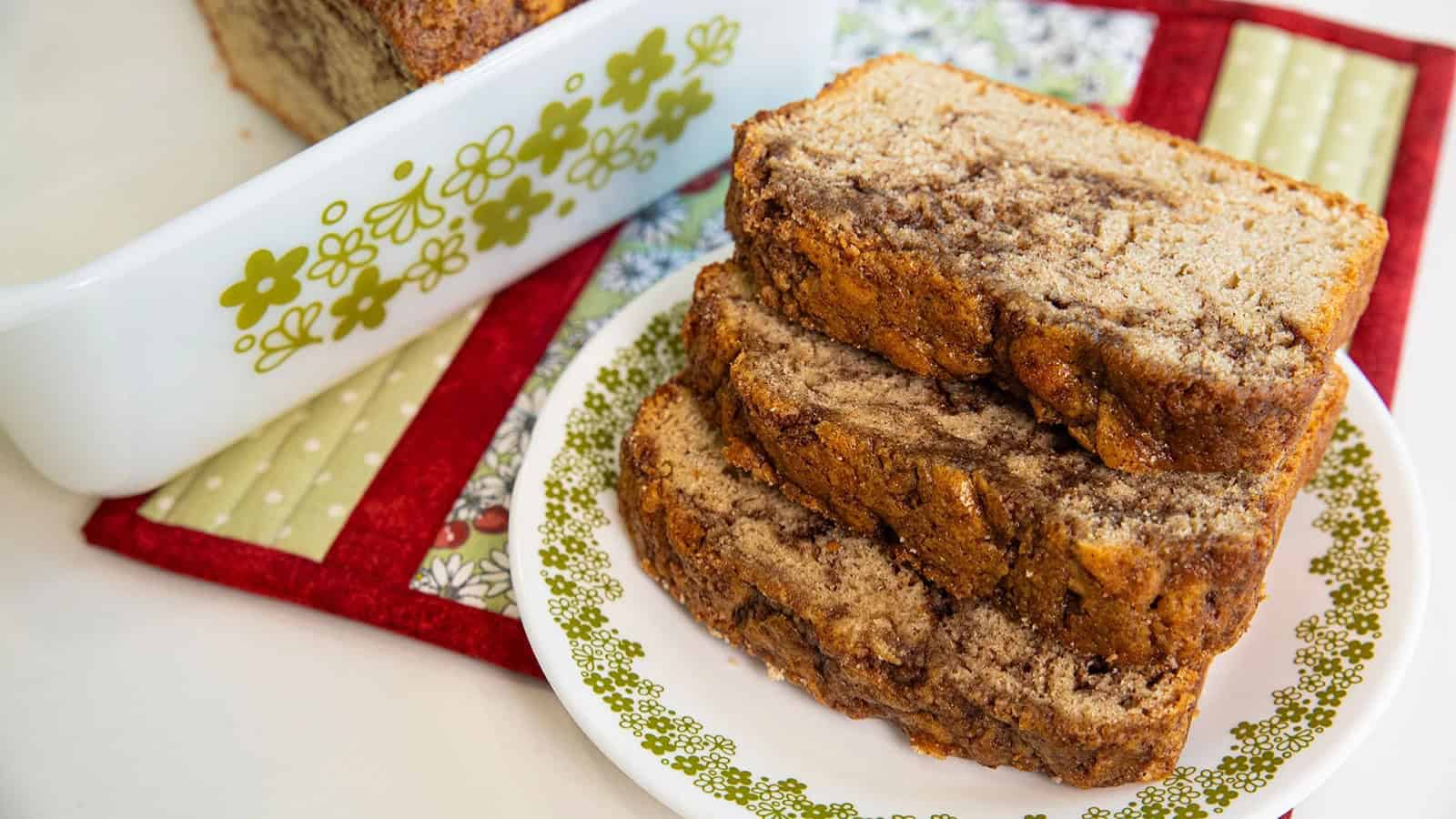 Three slices of banana bread stacked on a plate with a loaf pan in the background.