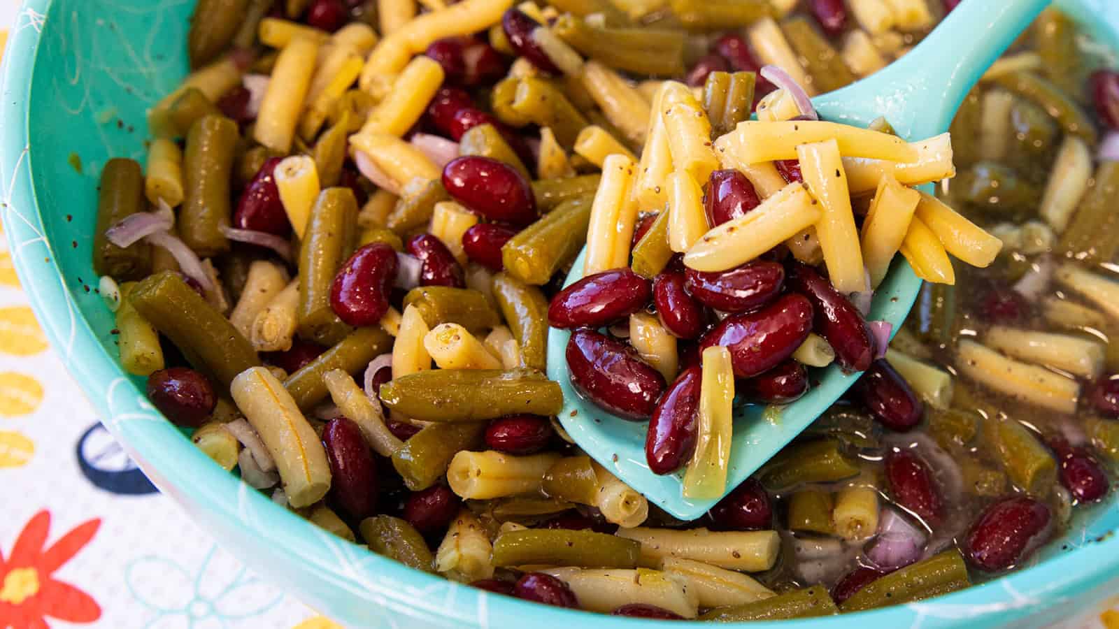 A close-up of three bean salad with green beans, wax beans, and kidney beans in a blue bowl with a spoon.