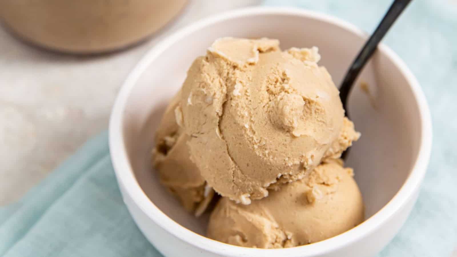 Coffee Ice Cream Ninja Creami in a glass bowl with a spoon and a glass jar with an ice cream scooper.