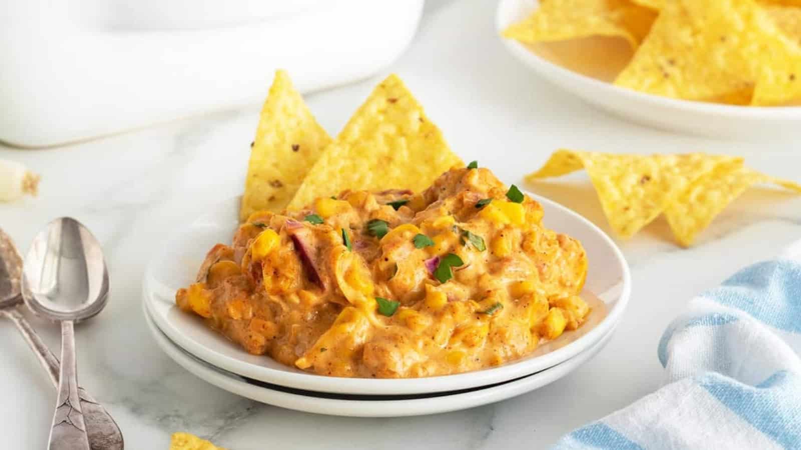 Creamy corn dip with herbs served on a small white plate, with tortilla chips on the side.
