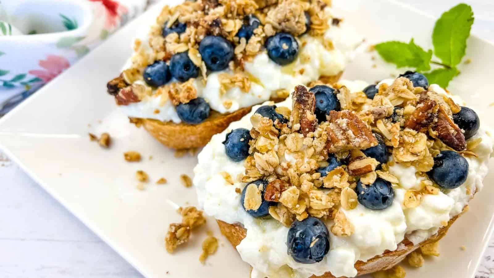 A plate of cottage cheese toast with blueberries, next to a honey dipper.