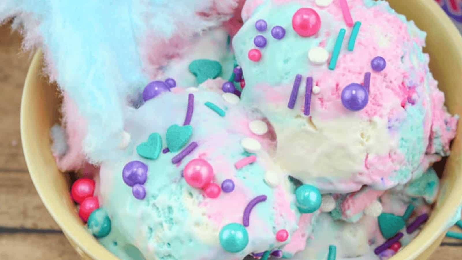 Colorful scoops of ice cream topped with pink, purple, and teal sprinkles in a bowl, with cotton candy.