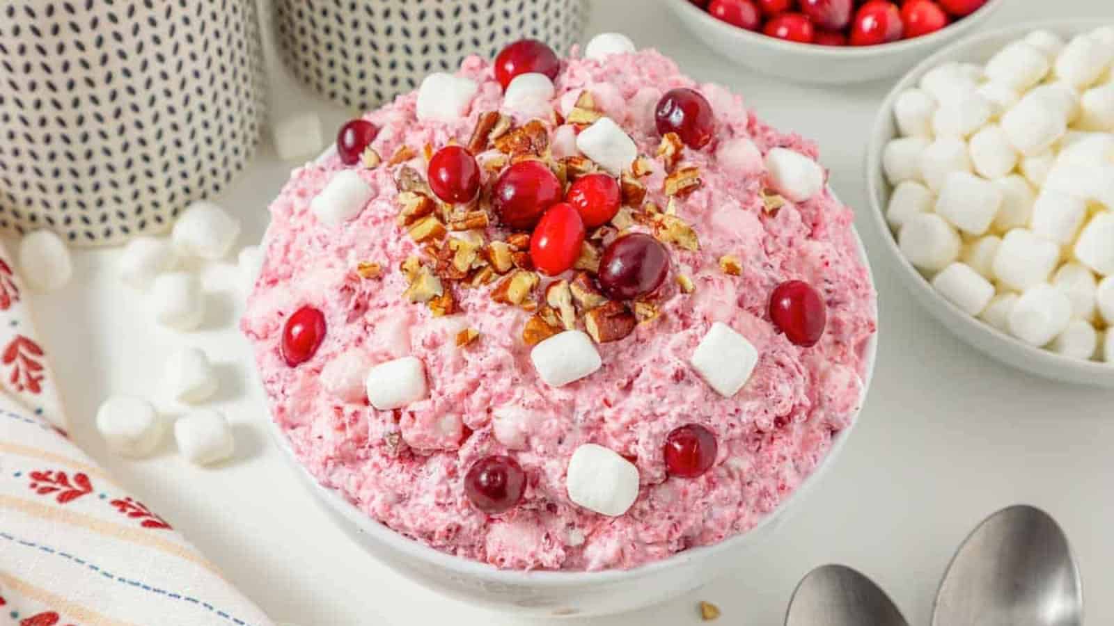 A bowl of pink cranberry salad topped with pecans, cranberries, and mini marshmallows.