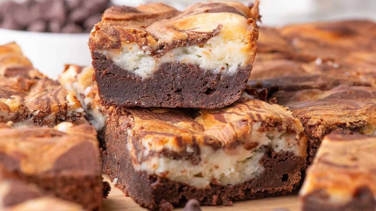 Fudgy brownies with a creamy cheesecake swirl, stacked on a wooden surface.