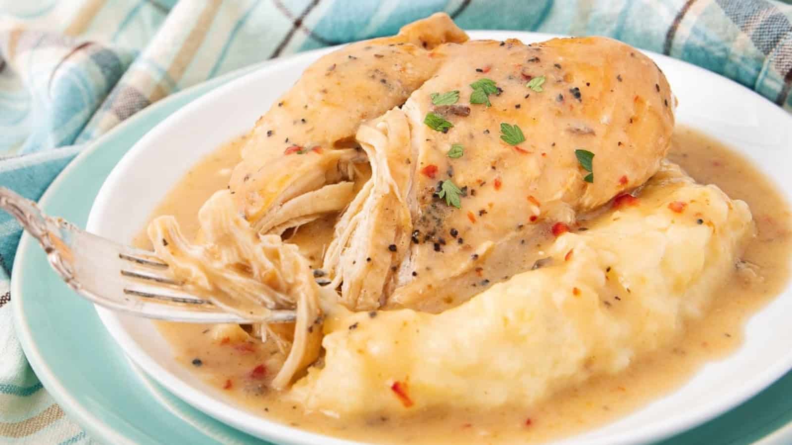 Shredded chicken breast with gravy and mashed potatoes on a white plate, garnished with herbs.