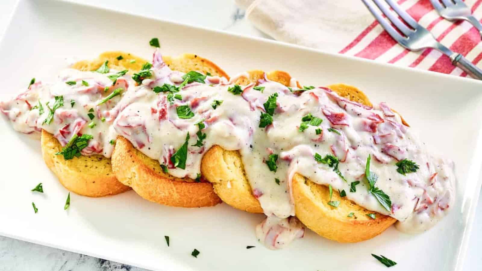 Toasted bread slices topped with creamy chipped beef gravy, garnished with chopped parsley on a white plate.