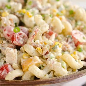 Bowl of creamy macaroni salad with cherry tomatoes, green onions, corn, and bacon pieces.