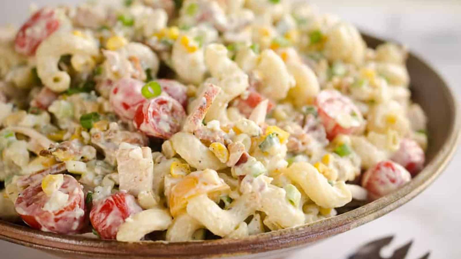 Bowl of creamy macaroni salad with cherry tomatoes, green onions, corn, and bacon pieces.