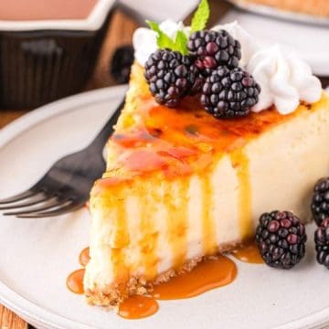 A slice of cheesecake topped with caramel sauce, blackberries, and whipped cream on a plate with a fork.