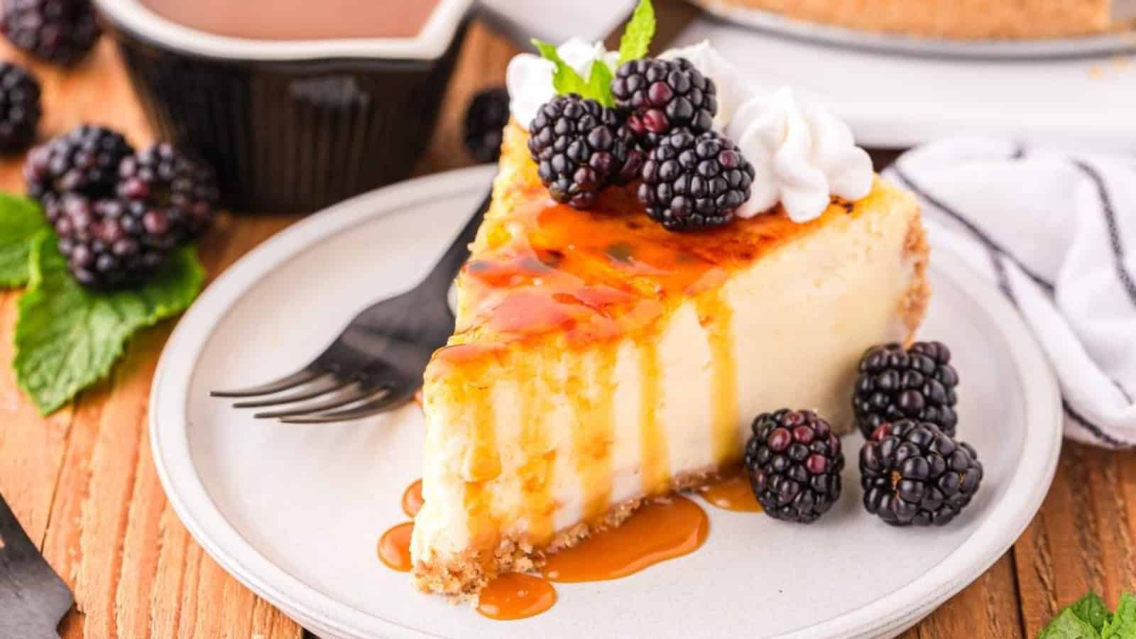 A slice of cheesecake topped with caramel sauce, blackberries, and whipped cream on a plate with a fork.