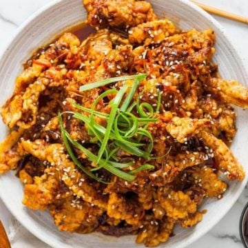 A plate of crispy fried chicken topped with sesame seeds and sliced green onions, with drinks on the side.