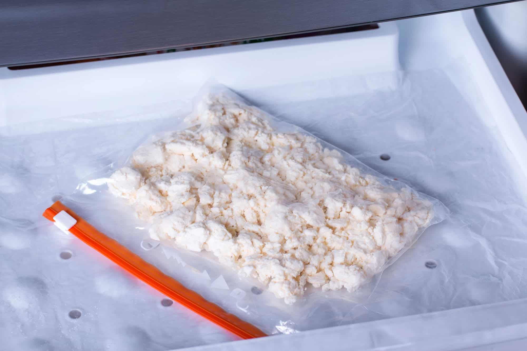A vacuum-sealed bag of white, crumbled food&mdash;illustrating how to freeze cheese&mdash;is placed inside a freezer drawer.
