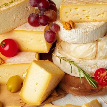 Assorted cheeses with grapes, olives, cherry tomatoes, walnuts, and rosemary on a wooden board-perfect for entertaining or learning how to freeze cheese for future gatherings.