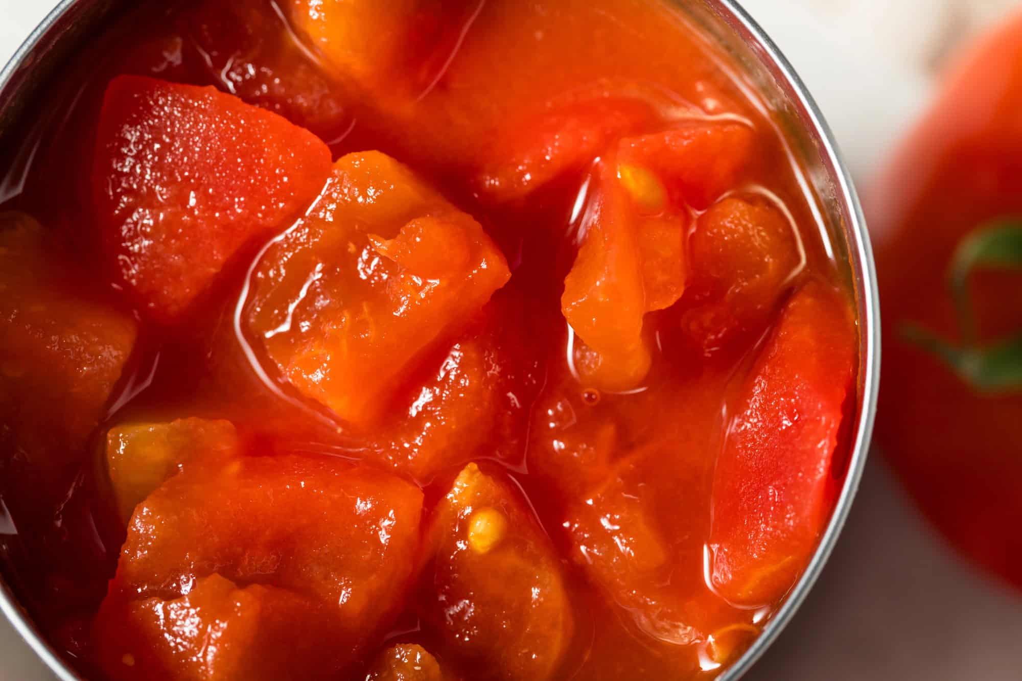 Close-up of canned diced tomatoes in tomato juice, showing juicy red tomato pieces and seeds.
