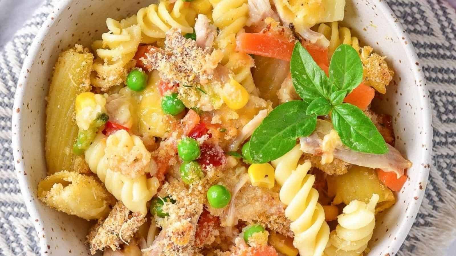A bowl of baked pasta with vegetables, bread crumbs, and a fresh basil garnish on top.