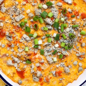 A bowl of buffalo chicken dip topped with blue cheese and green onions, served with tortilla chips.