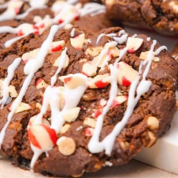 A close-up of chocolate cookies with white icing drizzle and chopped nuts on top.