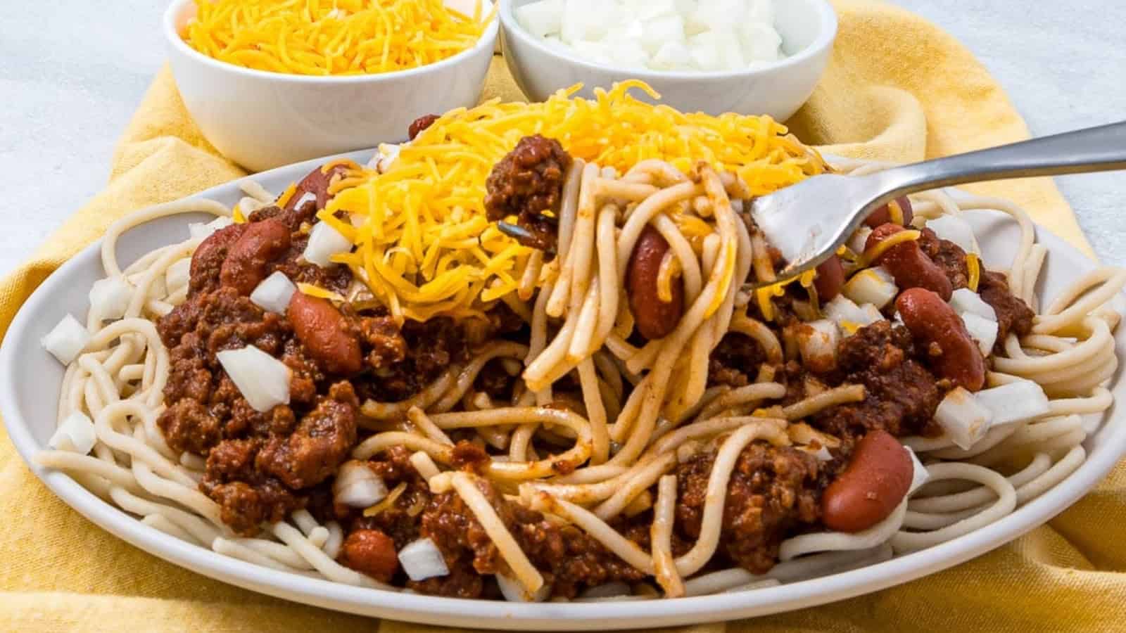 A plate of spaghetti topped with chili, kidney beans, chopped onions, and shredded cheddar cheese.