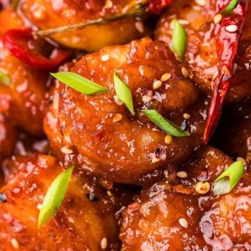 Close-up of spicy glazed shrimp with sliced green onions and sesame seeds served over white rice.