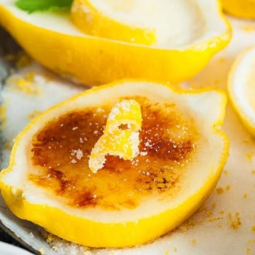 Caramelized lemon halves with sugar and zest, garnished with mint leaves on a white surface.