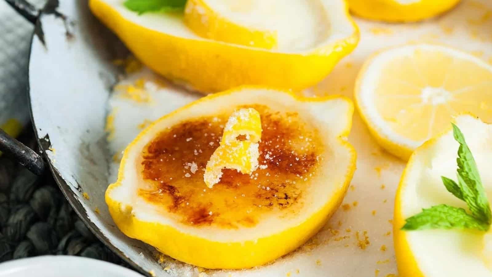 Caramelized lemon halves with sugar and zest, garnished with mint leaves on a white surface.