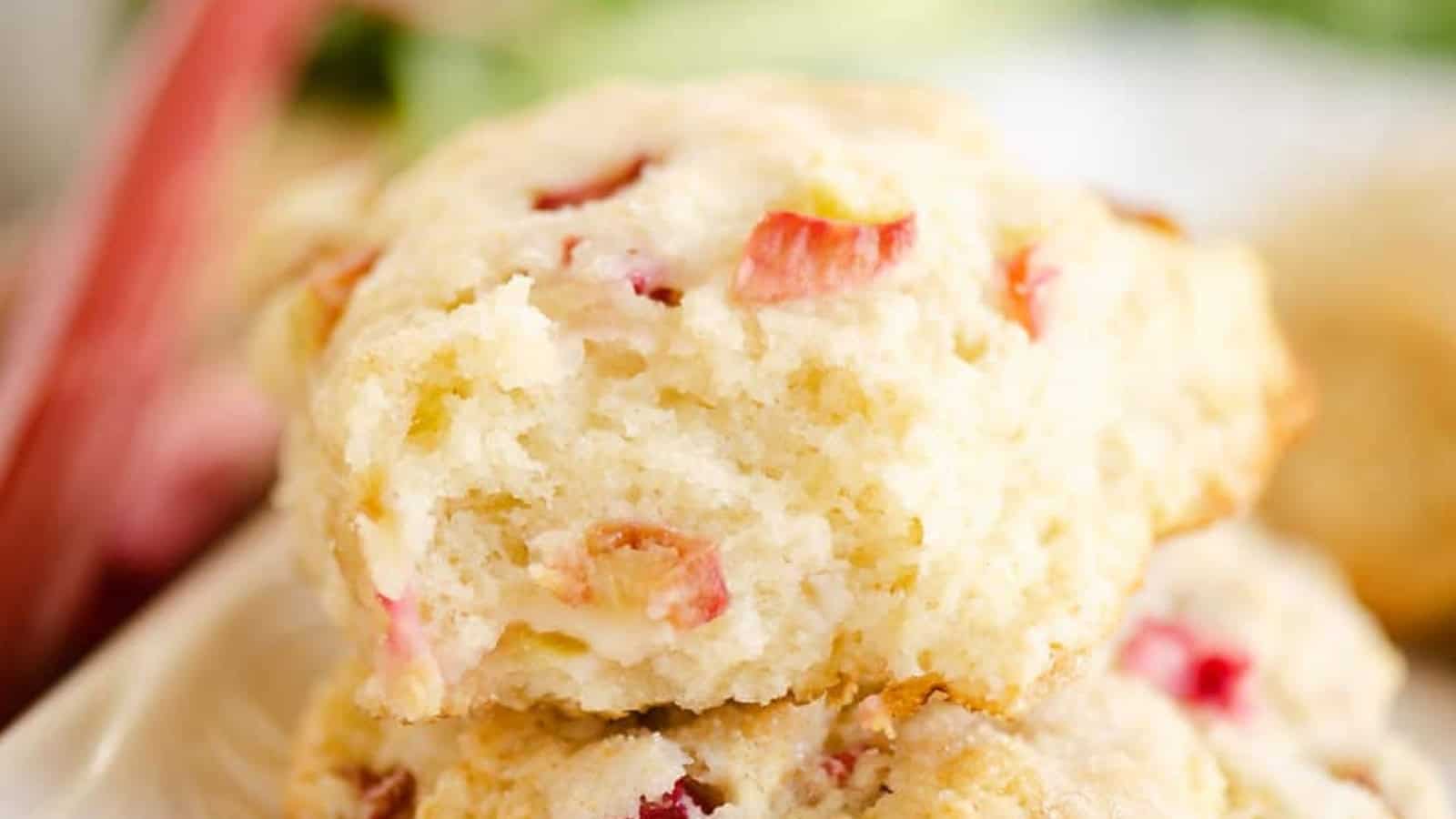 Close-up of a crumbly biscuit with pieces of pink rhubarb inside, stacked on another biscuit.