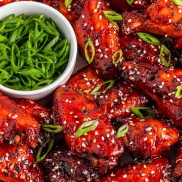 A plate of glazed chicken wings topped with sesame seeds and green onions, with sliced green onions on the side.