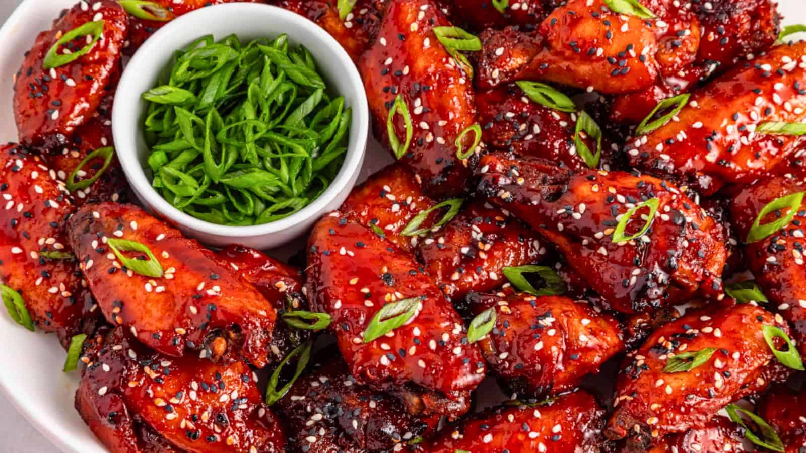 A plate of glazed chicken wings topped with sesame seeds and green onions, with sliced green onions on the side.