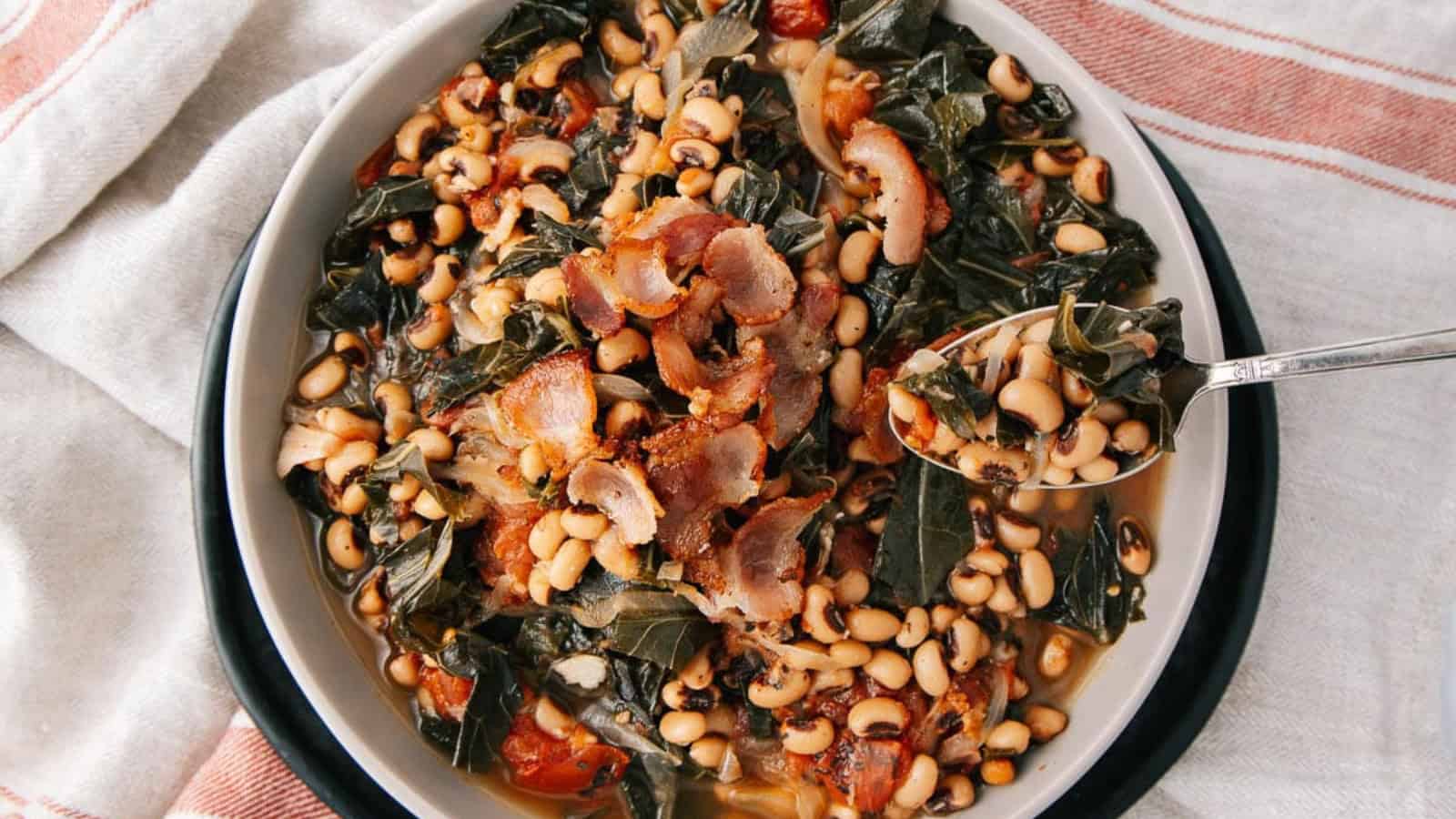 A bowl of black-eyed peas with greens and crispy bacon, with a spoon resting inside the bowl.