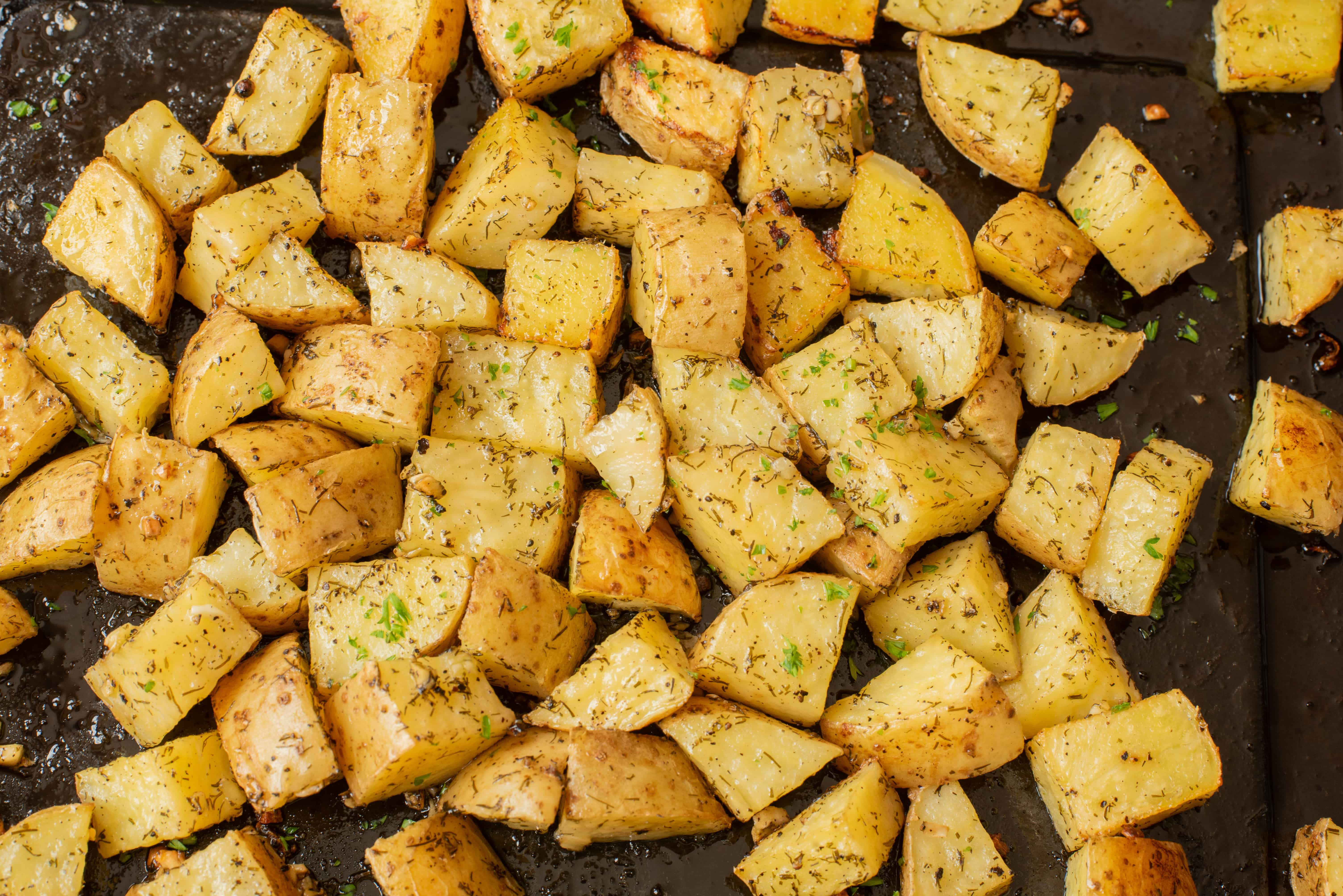 Cubed roasted potatoes with herbs on a dark baking sheet.