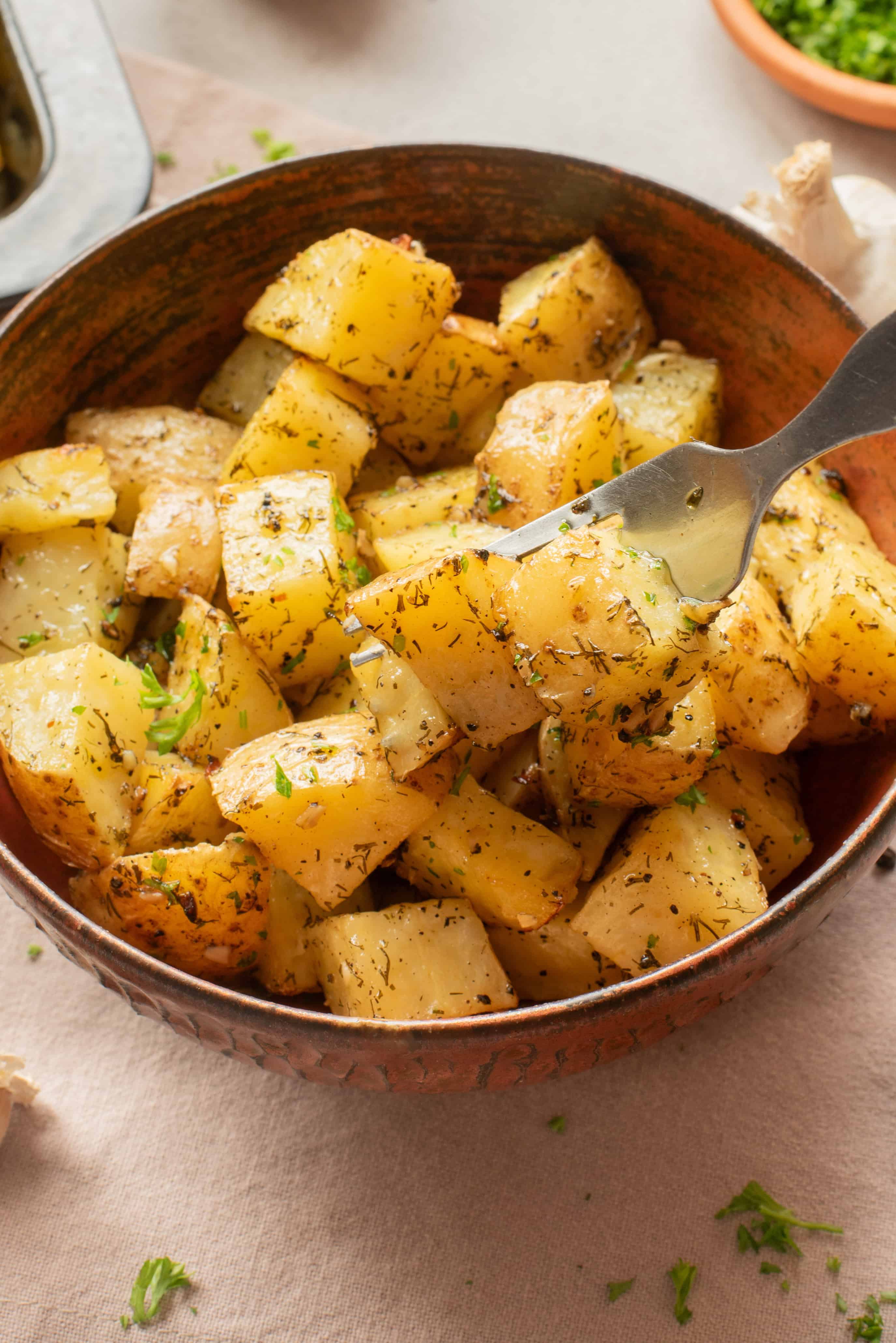 A bowl of roasted potato cubes with herbs, one piece is held up by a fork.