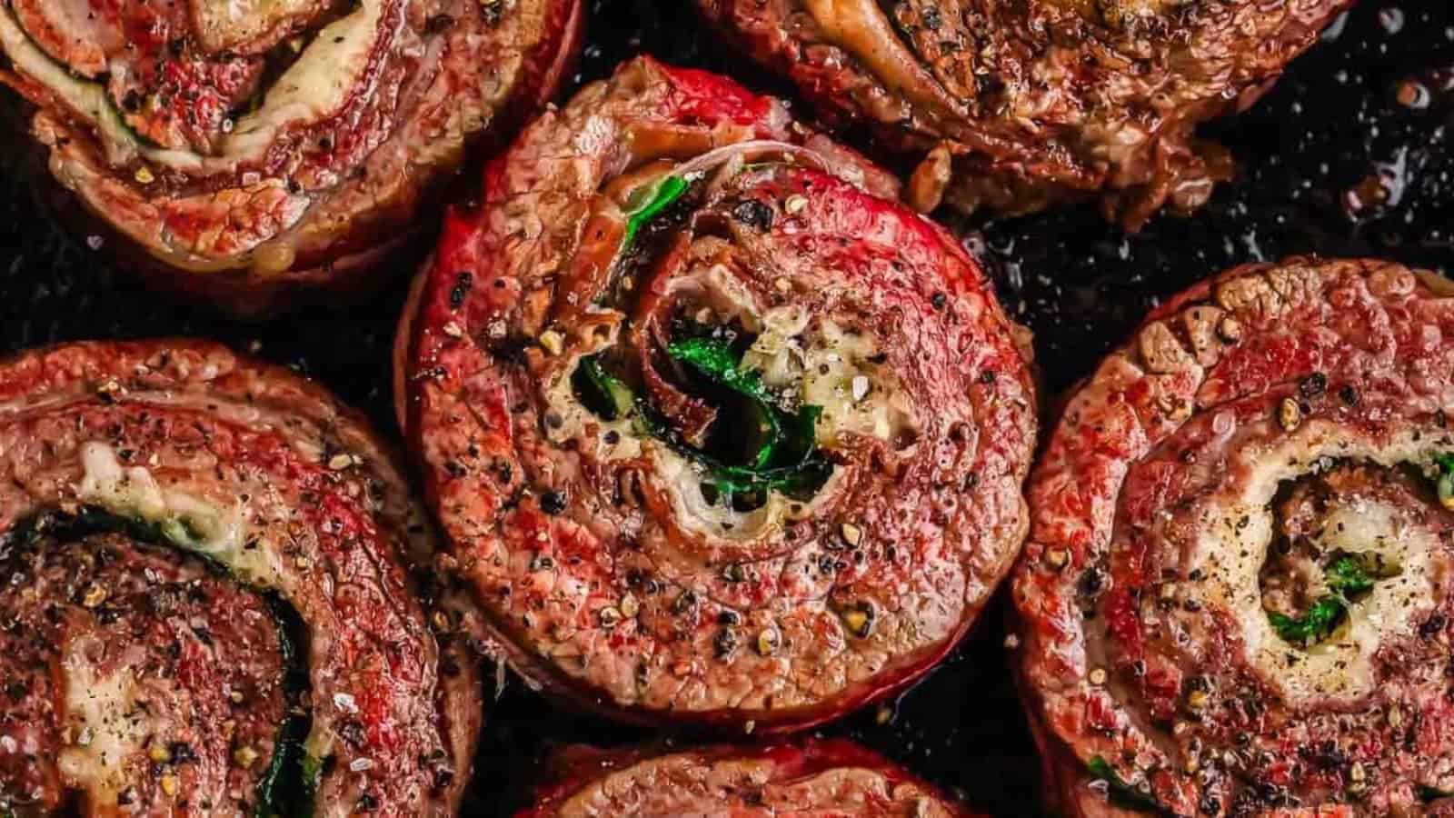Close-up of cooked beef pinwheels filled with herbs and seasonings, topped with cracked black pepper.