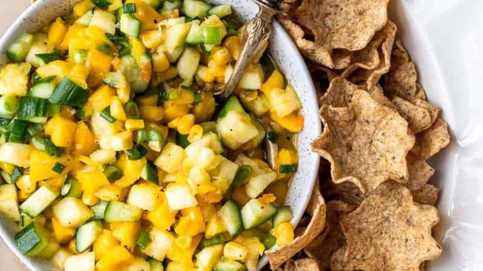 Bowl of pineapple salsa with diced cucumber and chips on the side.