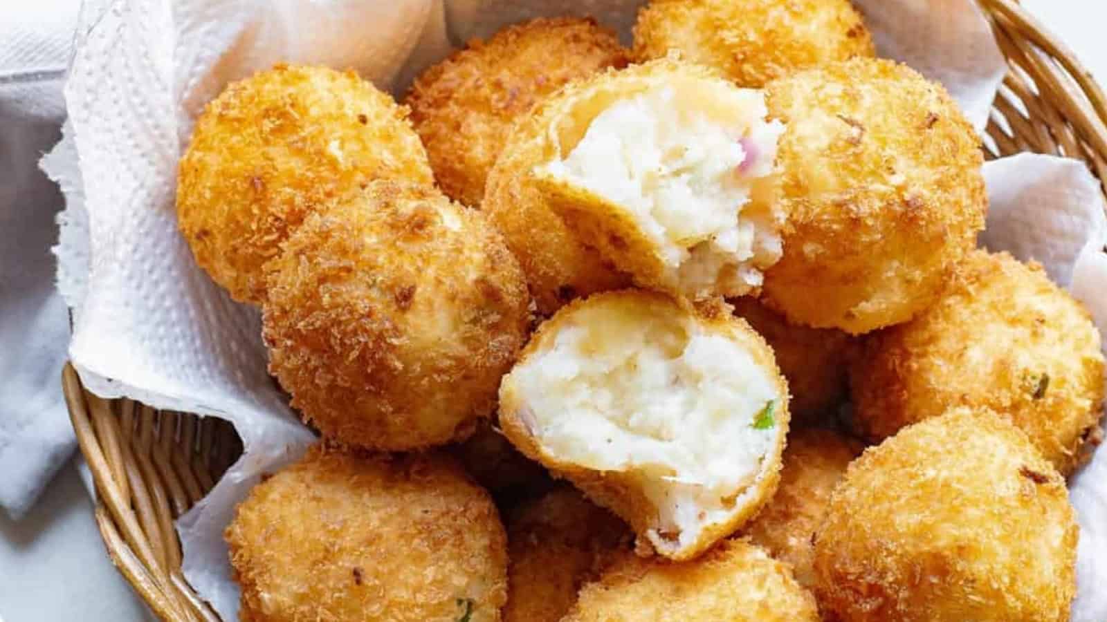 A basket of crispy, golden-brown mashed potato balls, with one broken open to show the creamy filling.